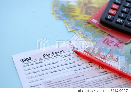 Swiss franc banknotes and tax form with pen on blue. The current francs money bills lies on tax form 126829627