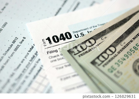 Hundred dollar bills and 1040 individual income tax return form blank close up Hundred dollar bills and 1040 individual income tax return form blank close up 126829631