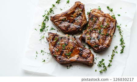 Grilled lamb chops on white parchment with sprigs of fresh herbs, seasoned and garnished, gourmet meal preparation. Culinary arts and fine dining concept 126830217