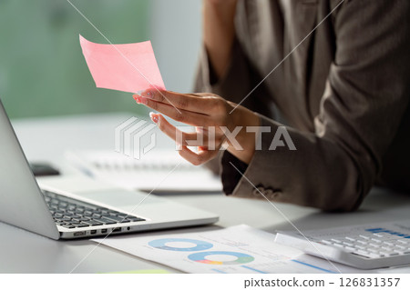Businesswoman reviewing notes while holding a sticky note in a modern office 126831357
