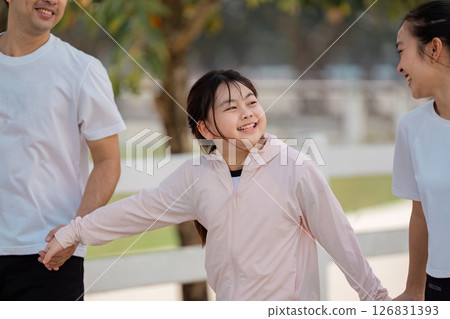 Family joyfully exercising together, daughter smiling as she holds hands with her parents during outdoor fun Family joyfully exercising together, daughter smiling as she holds hands with her parents during outdoor fun 126831393