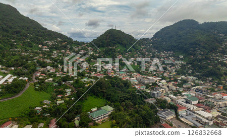 Dense residential area nestled between green hills with lush vegetation, various buildings, and winding roads visible. Seychelles, Mahe. Dense residential area nestled between green hills with lush vegetation, various buildings, and winding roads visible. Seychelles, Mahe. 126832668