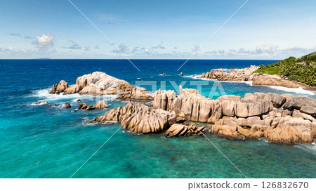Rocky coastline under a bright blue sky with some clouds in the distance. La Digue, Seychelles. Rocky coastline under a bright blue sky with some clouds in the distance. La Digue, Seychelles. 126832670
