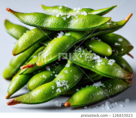 Fresh green edamame pods sprinkled with coarse salt, stacked in pile on light background 126833023