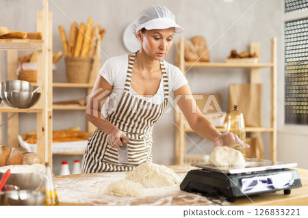 Woman in bakery cutting dough and weighing 126833221
