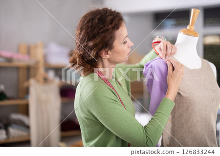 Woman tailor connects parts of dress on mannequin Woman tailor connects parts of dress on mannequin 126833244
