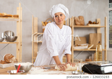 Adult female baker kneading dough on table 126833283