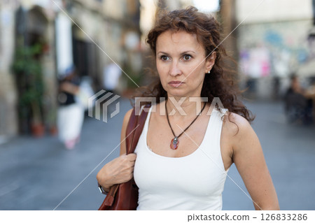 Woman with leather tote bag walking through summer city street 126833286