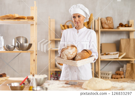 Young woman baker are standing near product range in bakery kitchen with basket loaf of bread Young woman baker are standing near product range in bakery kitchen with basket loaf of bread 126833297