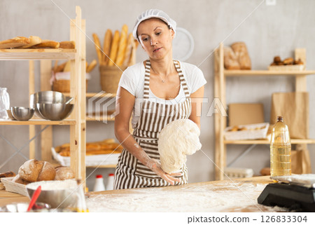 Working in bakery - woman kneads raw dough to make baguettes or croissants Working in bakery - woman kneads raw dough to make baguettes or croissants 126833304