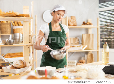 Adult woman baker whipping dough in bowl Adult woman baker whipping dough in bowl 126833309
