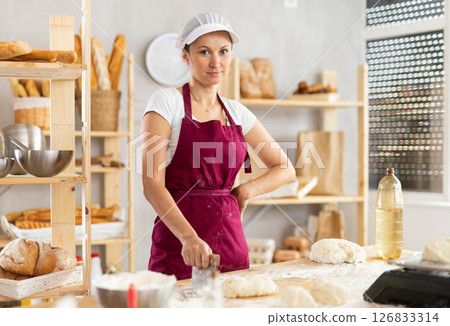 Portrait of female baker in uniform in interior of private bakery kitchen Portrait of female baker in uniform in interior of private bakery kitchen 126833314