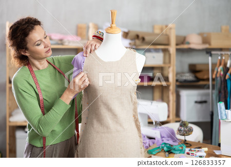 Dressmaker constructing custom dress on mannequin in sewing workshop 126833357