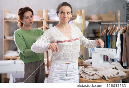 Woman tailor using measuring tape to measure clothes on girl in sewing workshop Woman tailor using measuring tape to measure clothes on girl in sewing workshop 126833383