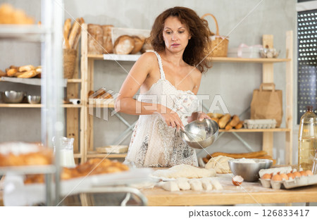 Woman whisking eggs and pouring batter on kitchen counter in bakery 126833417
