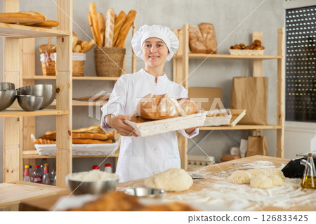 Young girl baker are standing near product range in bakery kitchen with basket loaf of bread Young girl baker are standing near product range in bakery kitchen with basket loaf of bread 126833425