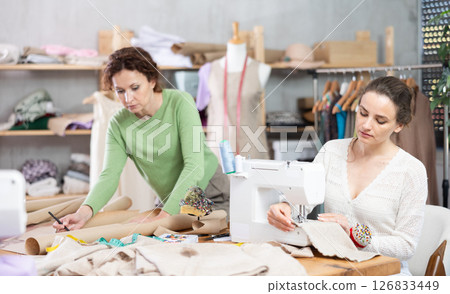 Woman tailor at work in cloth design shop. Companion draw dress pattern on paper 126833449