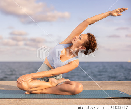 Yoga practice on embankment, female athlete fulfil carry out padmasana svastikasana, Siddhasana 126833517