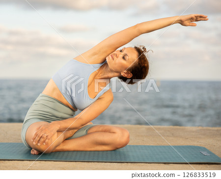 Yoga practice on embankment, female athlete fulfil carry out padmasana svastikasana, Siddhasana Yoga practice on embankment, female athlete fulfil carry out padmasana svastikasana, Siddhasana 126833519