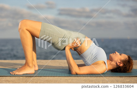 Yoga practice on embankment, female athlete fulfil carry out chatush padasana Yoga practice on embankment, female athlete fulfil carry out chatush padasana 126833604