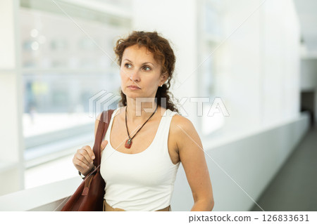 Woman with curly brown hair walking through bright hallway 126833631