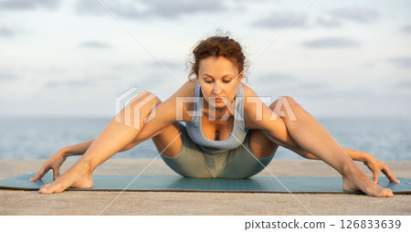 Yoga practice on embankment, female athlete fulfil carry out Upavishta Konasana Yoga practice on embankment, female athlete fulfil carry out Upavishta Konasana 126833639