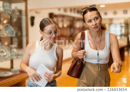 Young woman with teen daughter walk around museum, cookware zone. 126833654