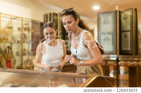 Young woman with teen daughter visitors stands near horizontal glass display case 126833655