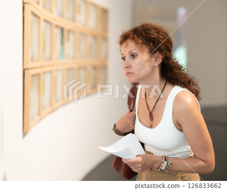 Middle-aged woman looking at pictures on wall in museum 126833662