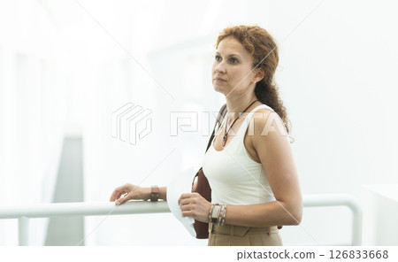 Middle-aged woman standing at handrails in public building Middle-aged woman standing at handrails in public building 126833668