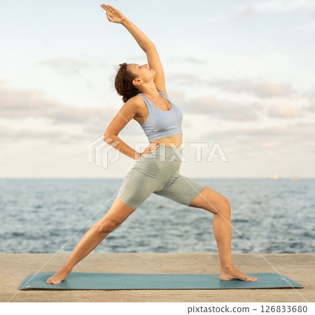 Athletic female yoga practitioner performing Garudasana on beach 126833680