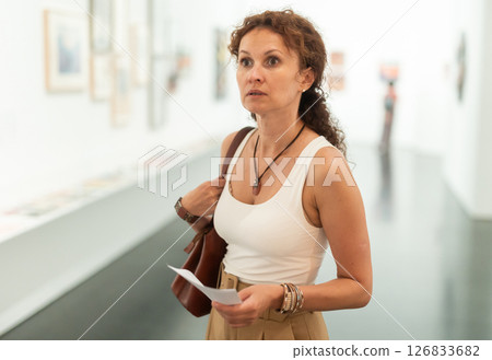 Middle-aged woman looking at pictures on wall in museum Middle-aged woman looking at pictures on wall in museum 126833682