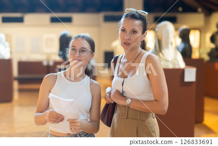 Young woman with teen daughter walk around museum, view sculpture in museum hall 126833691