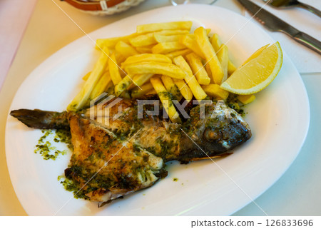 Baked in oven dorado fish with lemon and french fries served 126833696