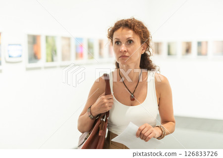 Middle-aged woman looking at pictures on wall in museum Middle-aged woman looking at pictures on wall in museum 126833726