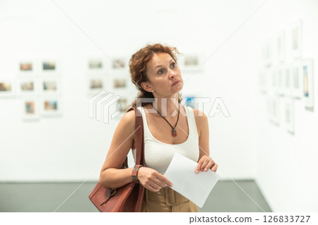 Thoughtful woman examining photographs on walls in art gallery 126833727