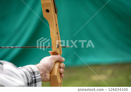 Close-Up of Hand Holding Wooden Bow with an Arrow on a Green Background 126834100