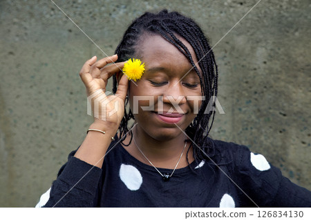 Smiling African Woman Holding Yellow Flower with Eyes Closed 126834130
