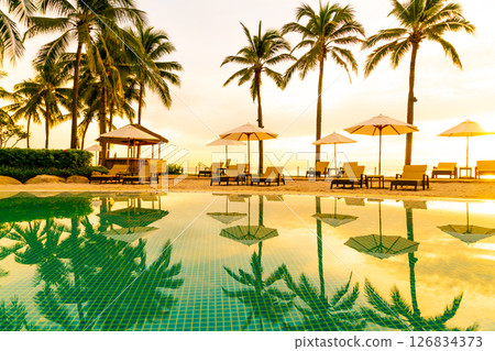 Umbrella and chair around swimming pool in hotel resort with sunrise in morning 126834373