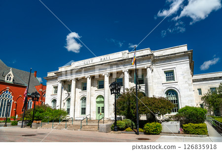 Neoclassical white stone city hall building in Pittsfield Massachusetts features tall columns and arched windows along a quiet civic square. The clear sky and sunlight highlight the architectural Neoclassical white stone city hall building in Pittsfield Massachusetts features tall columns and arched windows along a quiet civic square. The clear sky and sunlight highlight the architectural 126835918