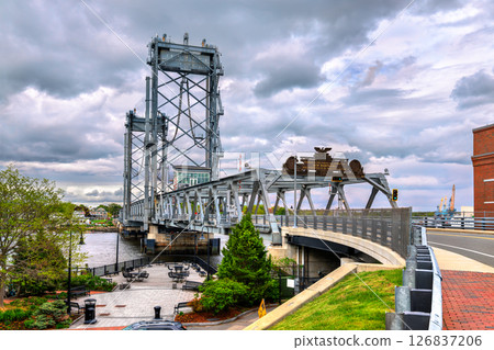 View of Memorial Bridge spanning the Piscataqua River between Portsmouth, New Hampshire and Kittery, Maine, featuring steel trusses, a lift section, and a small riverside plaza under cloudy skies 126837206