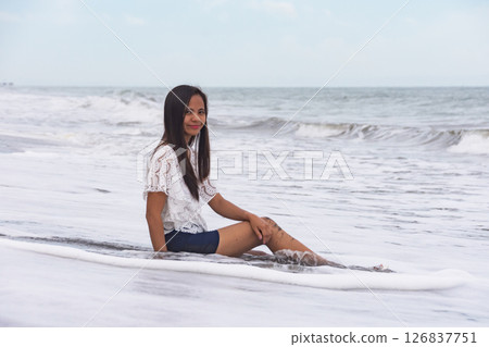 Happy woman sitting on the beach with waves in the background 126837751