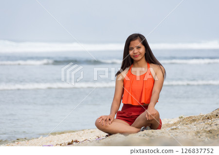 Happy woman sitting on the beach with waves in the background 126837752