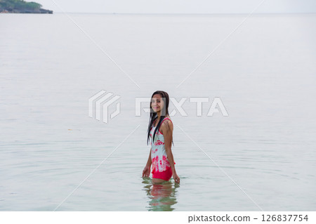 Young woman in swimsuit stands waist-deep in clear tropical sea water early in the morning Young woman in swimsuit stands waist-deep in clear tropical sea water early in the morning 126837754