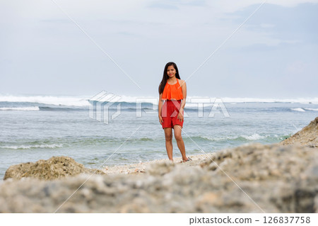 Young woman standing by the ocean with rocks behind, sea raging 126837758