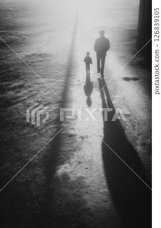 Child and adult walking hand in hand on a misty path, casting long shadows in the soft morning light 126839105