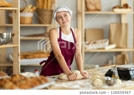 Teenage girl baker kneads the dough in bakery 126839367