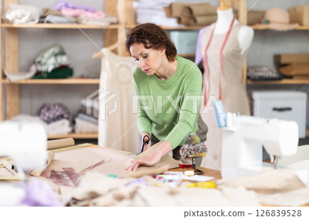 Female tailor cutting paper with scissors, cutting out the outline of pattern for a dress 126839528