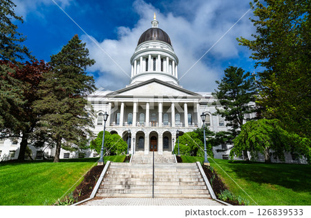 Classical white granite capitol building with a prominent dome and columned portico, surrounded by manicured green lawns and tall trees in Augusta, Maine, USA 126839533