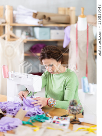 Female seamstress working on sewing machine in workshop Female seamstress working on sewing machine in workshop 126839548
